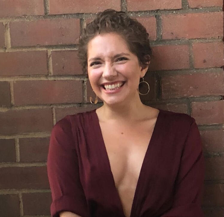 Yael from the torso up with short brown hair, hoops, and a red dress