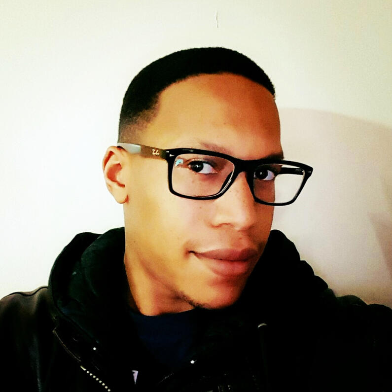 Darren, shoulders on up, with short black hair, wearing rectangular black glasses and a black hoody