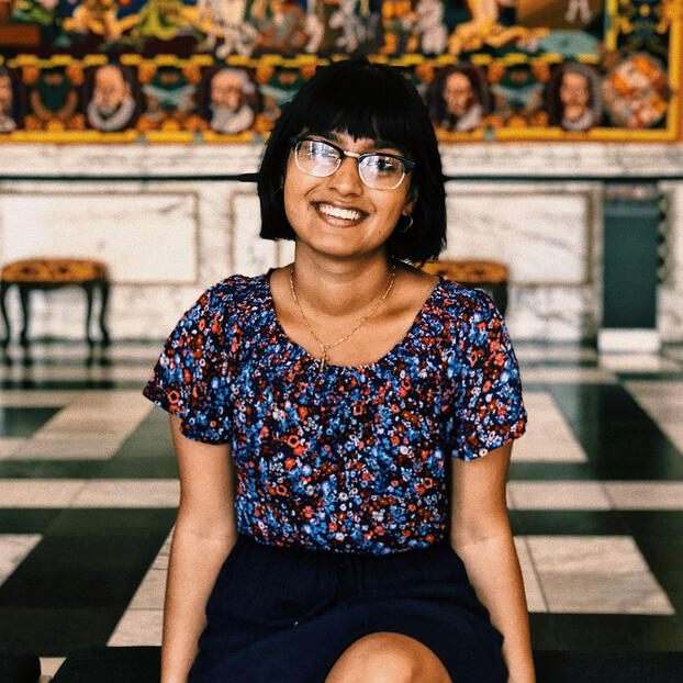 Christine sitting with short straight black bob hair, flowery short sleeves shirt, and black skirt