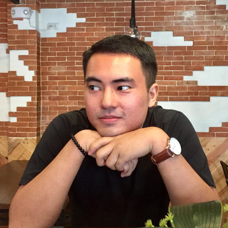 Yuki from wait up, hands on table and crossed under his chin. Short dark straight hair and looking to the side with watch on wrist